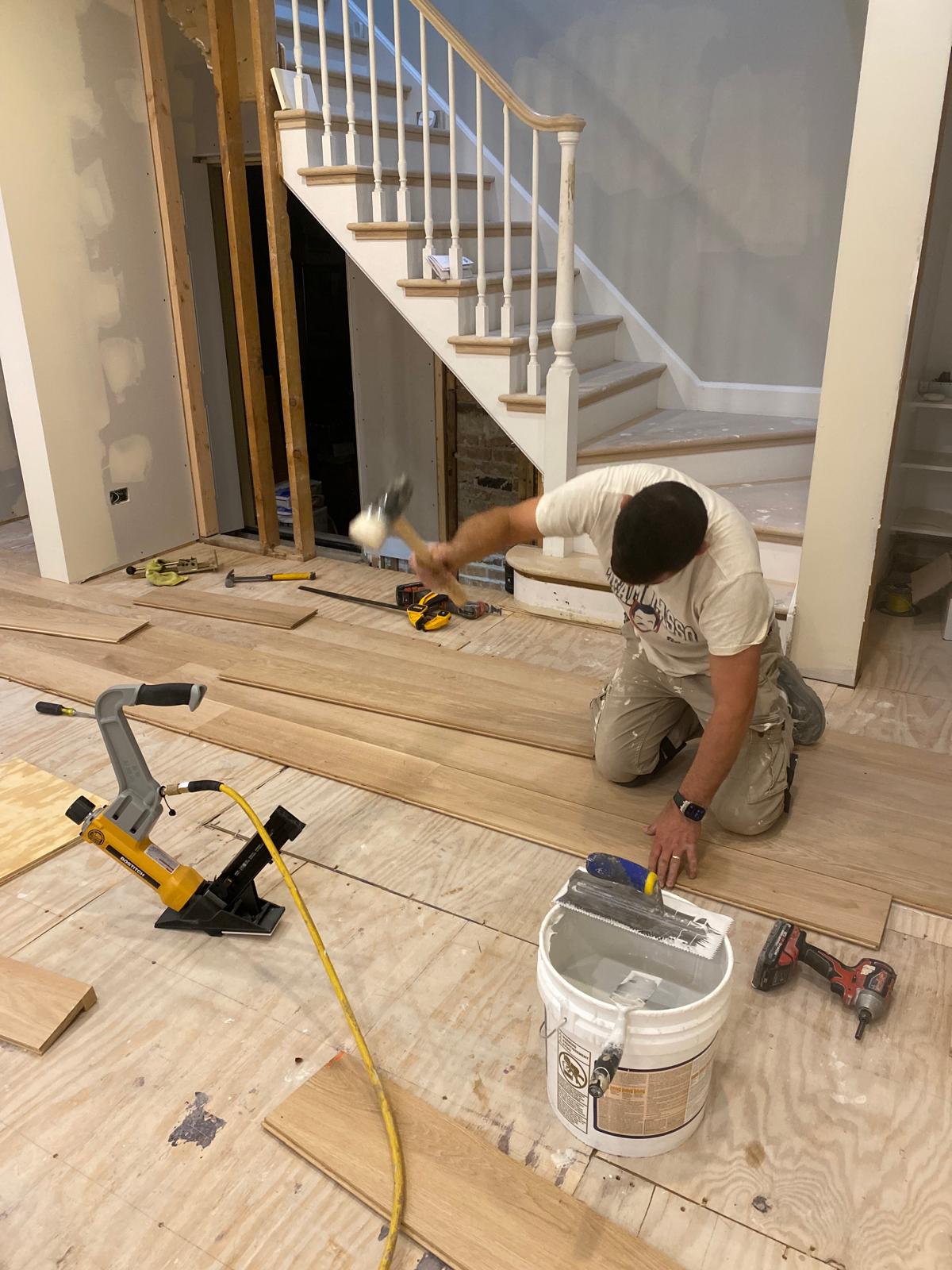 Hardworking construction worker laying new hardwood flooring in a home remodeling project.